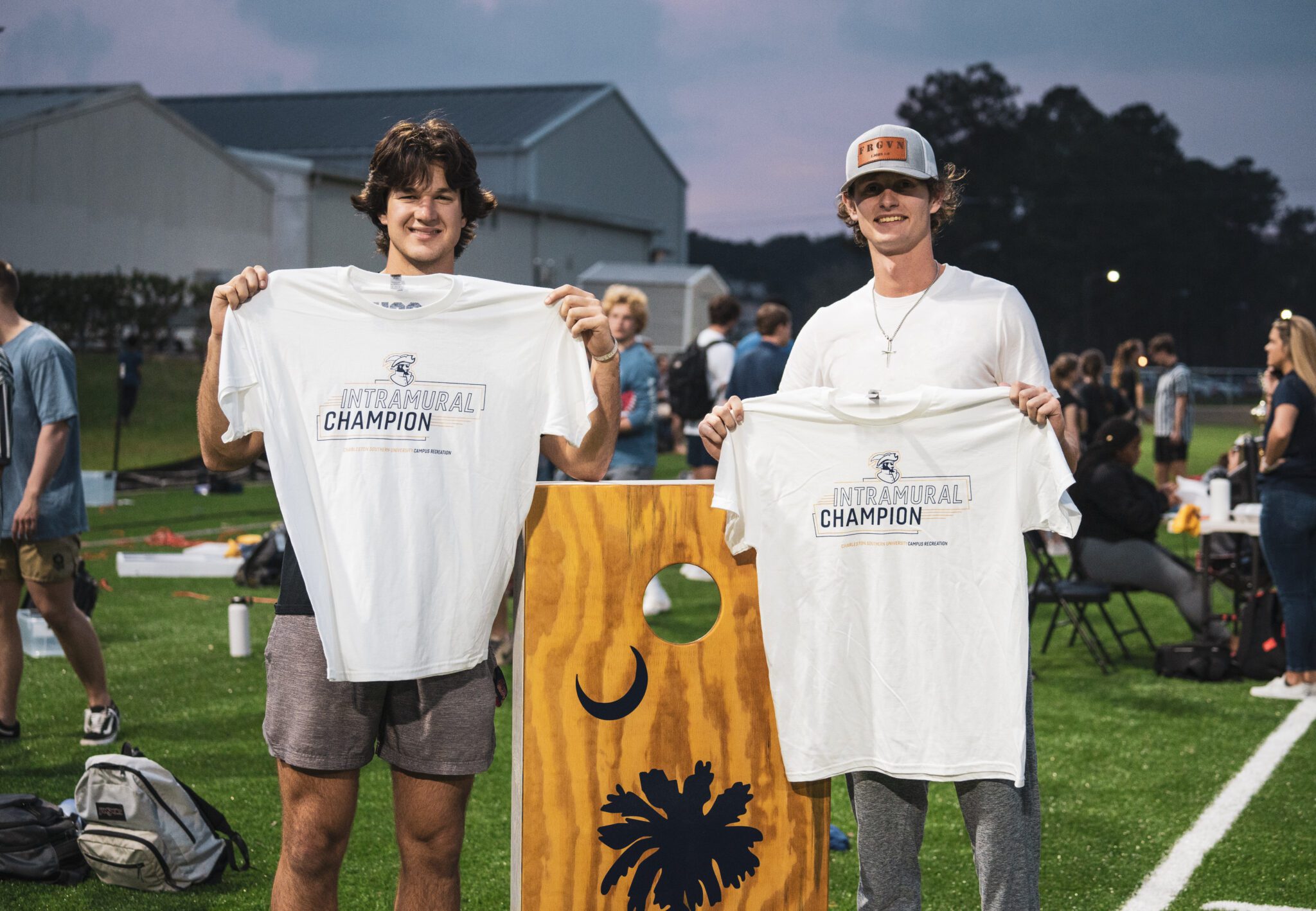 Two students holding teeshirts in front of a corn hole representing Charleston Southern's Intramurals.